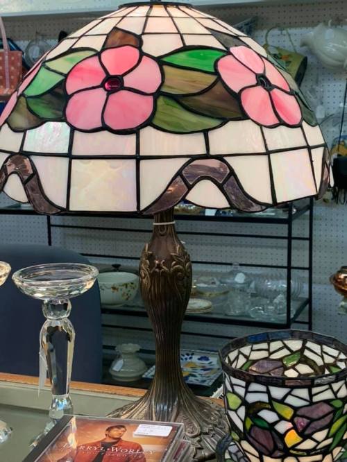 A stained glass lamp with a floral design, featuring pink flowers and a bronze base, displayed among various items.