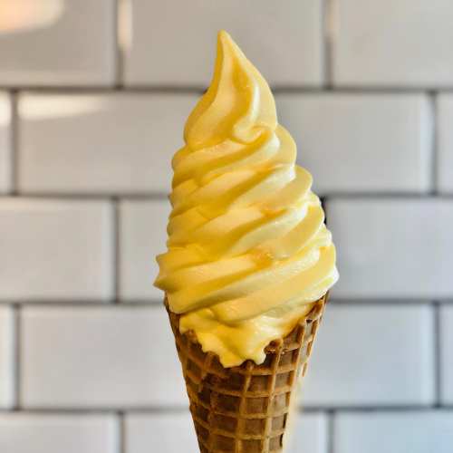A close-up of a soft-serve ice cream cone with a creamy swirl on top, set against a tiled background.