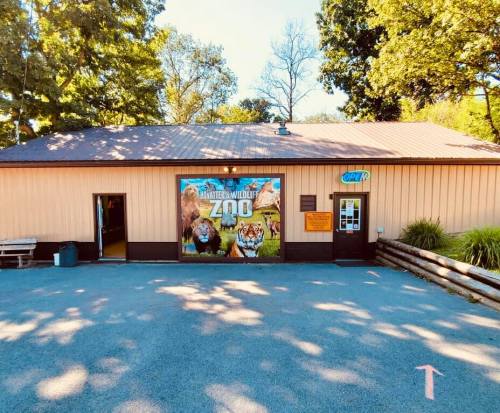 A building with a sign reading "Wildlife Zoo" featuring animal images, surrounded by trees and a clear blue sky.