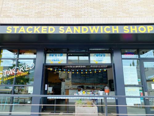 Exterior of Stacked Sandwich Shop with a bright sign, open doors, and a welcoming atmosphere.