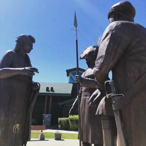 Three bronze statues depicting historical figures engaged in conversation, set against a clear blue sky.