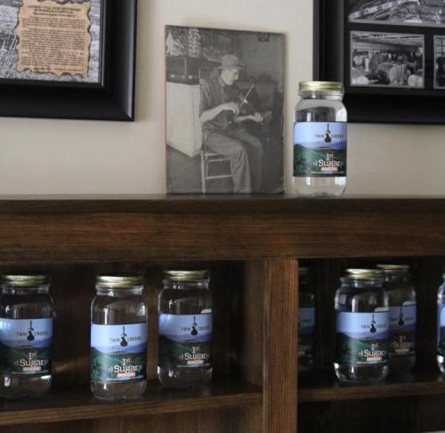 A wooden shelf displays jars labeled "Sugar" alongside framed black-and-white photos of a man playing the violin.