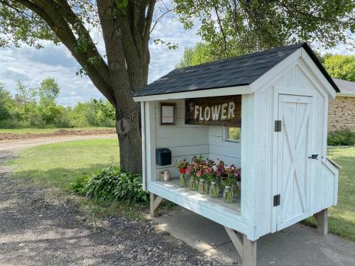 A small white shed with a sign reading "FLOWER" displays fresh flower bouquets on a sunny day.