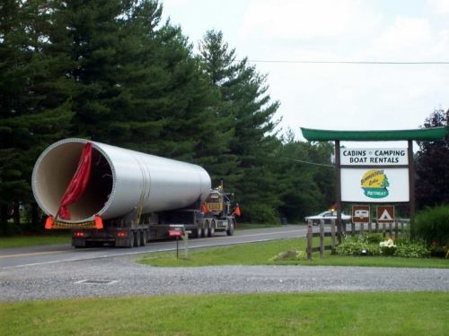 A large truck transporting a cylindrical object drives past a sign for cabins, camping, and boat rentals.
