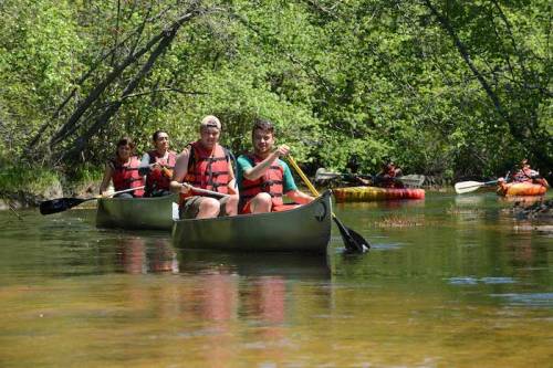 A group of people in canoes paddling on a calm river surrounded by lush greenery.