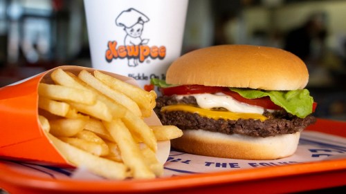 A cheeseburger with lettuce, tomato, and mayo, served with a side of fries and a drink in a fast-food setting.