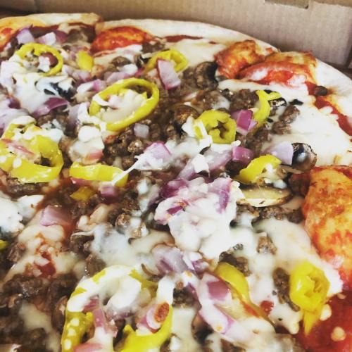 Close-up of a pizza topped with cheese, ground beef, onions, olives, and yellow peppers in a pizza box.