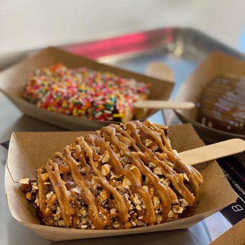 Three dessert pops on a tray: one covered in sprinkles, one in chocolate, and one with caramel and nuts.