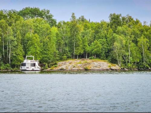 A boat docked near a rocky shore surrounded by lush green trees and calm water.