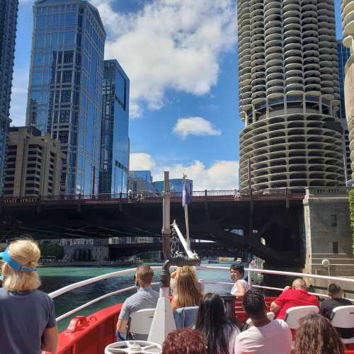 View from a boat on a river, showcasing city skyscrapers and a bridge under a bright blue sky with fluffy clouds.