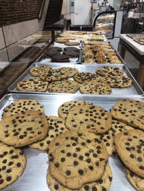 A display of freshly baked cookies, including large chocolate chip cookies and various other treats on metal trays.