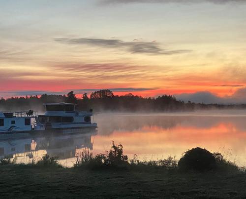 A serene lake at sunrise, with mist rising and a houseboat reflecting the colorful sky.