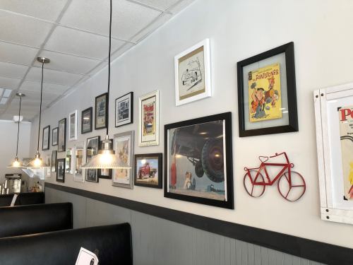 A diner wall adorned with various framed vintage photos, artwork, and a red bicycle decoration.
