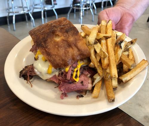 A plate with a sandwich filled with meat and melted cheese, accompanied by a side of crispy French fries.