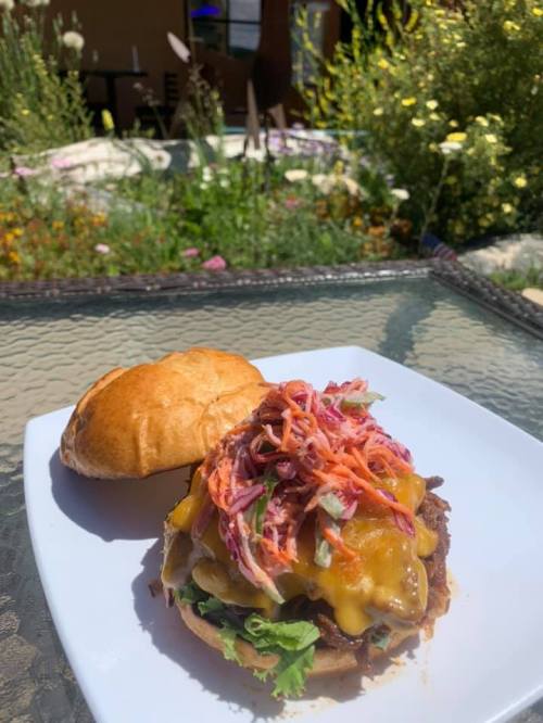 A delicious cheeseburger topped with colorful slaw, served on a plate with a soft bun, set against a garden backdrop.