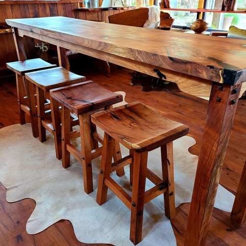 A rustic wooden bar with four matching stools on a cowhide rug in a cozy interior setting.