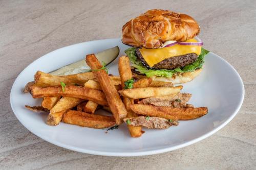 A plate with a cheeseburger topped with lettuce, onion, and a pickle, accompanied by crispy golden fries.