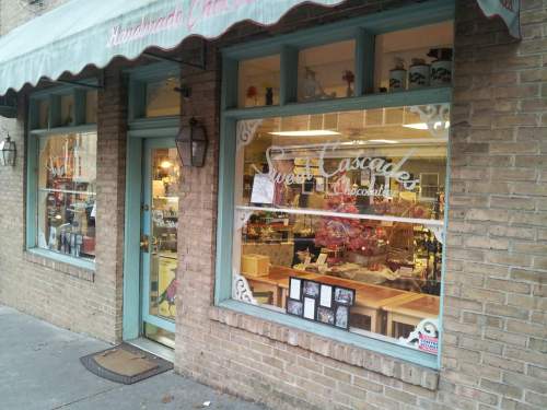 A charming storefront with large windows displaying colorful treats and a sign reading "Sweet Cascades Chocolates."