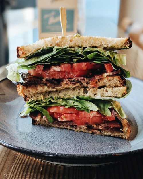 A stacked sandwich with layers of lettuce, tomato, and meat, served on a blue plate with a toothpick on top.