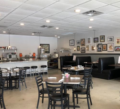 A cozy diner interior with black chairs, tables, and a counter, featuring framed artwork on the walls.