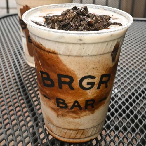 A large cup of milkshake topped with crushed cookies, featuring a mix of chocolate and vanilla swirls.