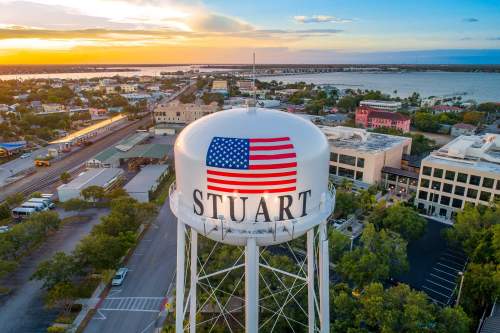 Aerial view of a water tower in Stuart, Florida, featuring an American flag and the town's name illuminated at sunset.