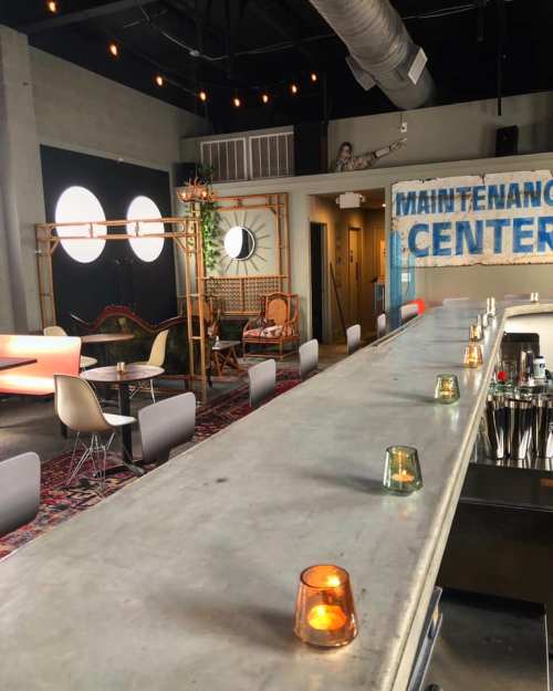 A modern bar area with a concrete counter, colorful candles, and eclectic seating in a stylish, industrial space.