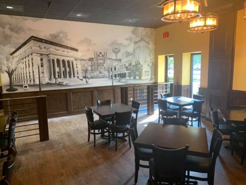 Interior of a restaurant featuring wooden tables, chairs, and a mural of a cityscape on the wall.