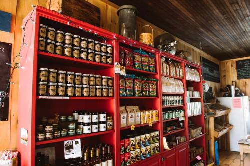 A red wooden shelf filled with jars, bottles, and bags of various food products in a rustic store setting.