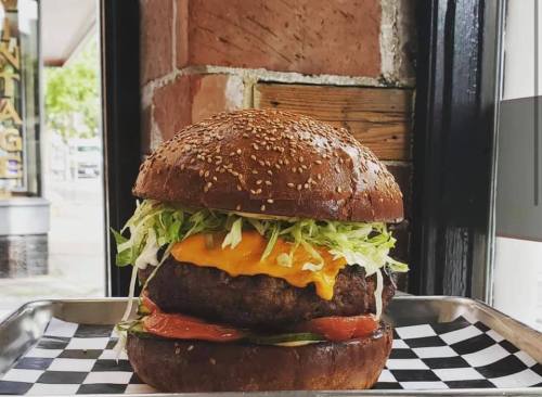 A large sesame seed bun burger stacked with lettuce, tomato, cheese, and a juicy beef patty on a checkered tray.
