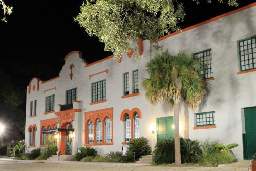 Historic building at night, featuring white walls, orange accents, green windows, and palm trees in the foreground.
