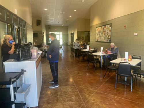 A spacious restaurant interior with tables, a counter, and customers dining while wearing masks.