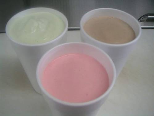 Three cups of creamy desserts: one green, one pink, and one brown, arranged in a row on a countertop.