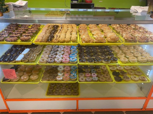 A display case filled with various donuts, including glazed, chocolate, and sprinkled varieties, arranged on yellow trays.