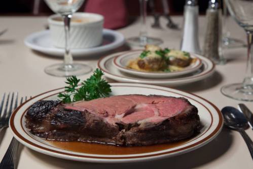 A plate of medium-rare prime rib with a garnish of parsley, served with side dishes and dining utensils in the background.