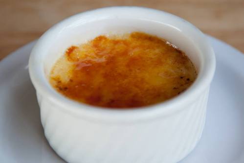 A creamy dessert in a white ramekin with a caramelized sugar top, sitting on a white plate.