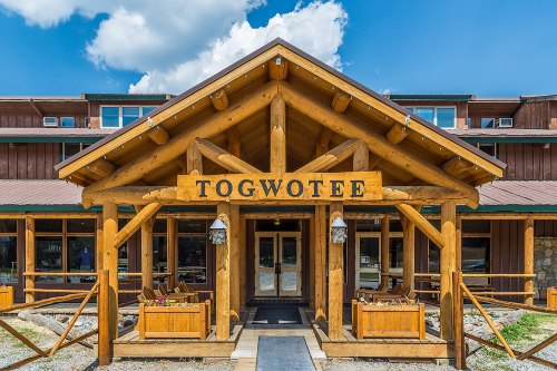 Entrance of Togwotee Lodge with wooden beams, a sign, and a clear blue sky in the background.