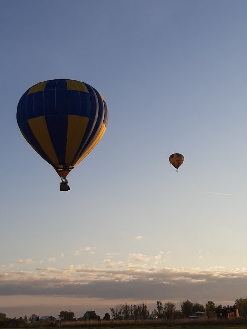 Two colorful hot air balloons float in the sky during sunset, with a serene landscape below.