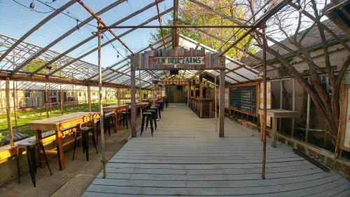 A rustic greenhouse with wooden tables and chairs, featuring a bar area and greenery outside.