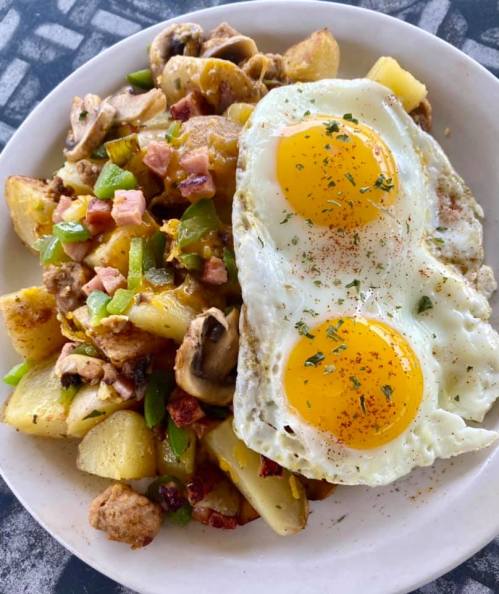 A plate of breakfast featuring golden potatoes, mushrooms, green peppers, ham, and two sunny-side-up eggs.