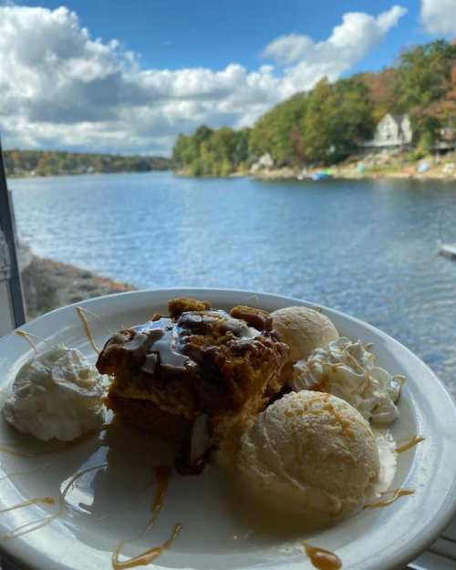 A plate with dessert featuring cake, ice cream, and whipped cream, set against a scenic lakeside view.