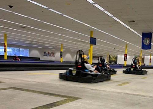 Go-karts racing on an indoor track with yellow pillars and flags in the background.