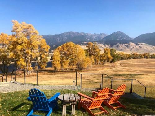 Colorful Adirondack chairs overlook a scenic landscape of golden trees and mountains under a clear blue sky.