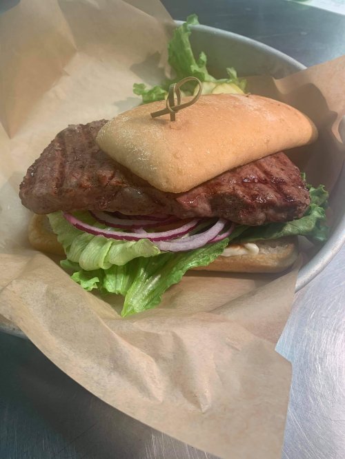 A grilled sandwich with a beef patty, lettuce, red onion, and a soft bun, served on parchment paper.