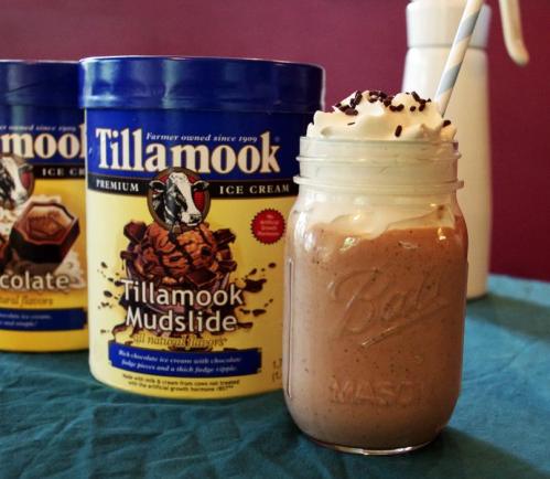 A mason jar filled with a chocolate milkshake topped with whipped cream and chocolate sprinkles, next to Tillamook ice cream.