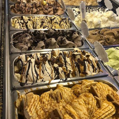 A variety of gelato flavors displayed in metal trays, featuring swirls of chocolate, caramel, and toppings.