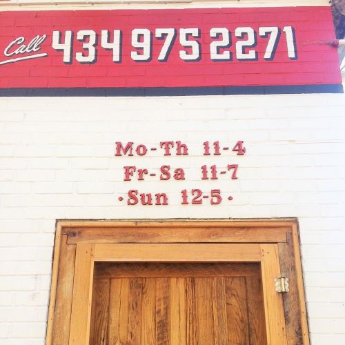 A red and white wall with a phone number and business hours displayed in bold lettering above a wooden door.