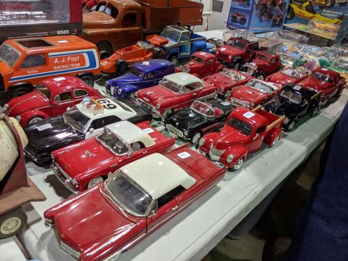 A collection of vintage toy cars displayed on a table, featuring various models and colors, mostly in red and black.