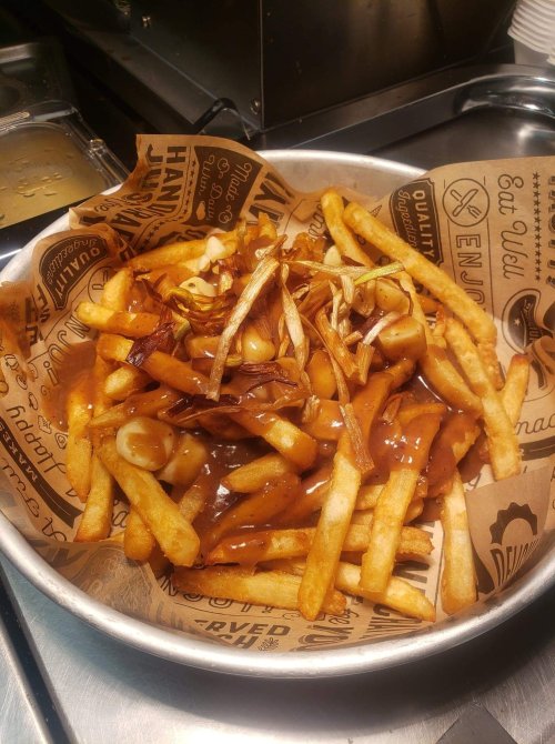 A metal bowl filled with fries topped with gravy, cheese curds, and crispy onions on a patterned paper liner.