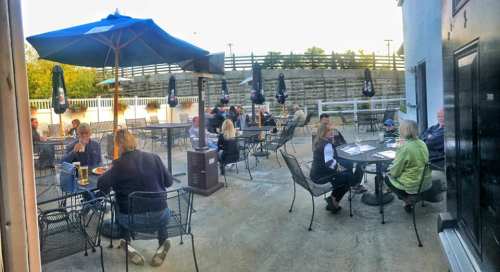 Outdoor dining area with people seated at tables under umbrellas, enjoying meals in a relaxed atmosphere.